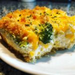 A close-up of a serving of chicken broccoli rice casserole, featuring a creamy interior, melted cheddar cheese, and a golden crumb topping.