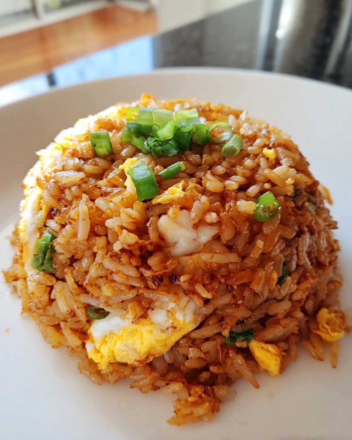 A close-up of a perfectly mounded serving of savory chicken fried rice, topped with fresh green onions.