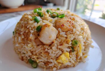 A dome-shaped serving of golden brown chicken fried rice topped with seared scallops and green onions.