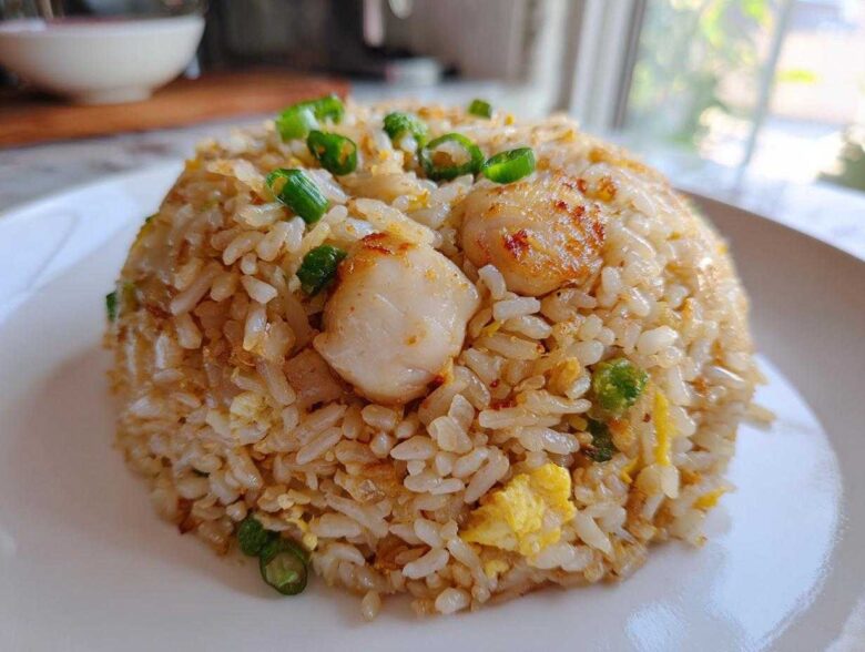 A dome-shaped serving of golden brown chicken fried rice topped with seared scallops and green onions.