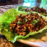 A close-up of a crisp lettuce cup filled with savory, saucy chicken lettuce wraps mixture, garnished with green onions.