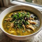 Close-up of a bowl of vibrant green chicken poblano soup recipe, topped with shredded chicken, black beans, and fresh cilantro.