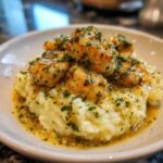 Close-up of chicken scampi pieces served over creamy garlic parmesan rice, drizzled with butter sauce.