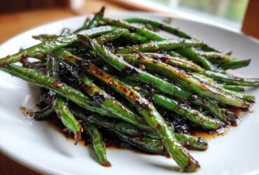 Close-up of bright green beans coated in a dark, glossy chinese green beans with garlic sauce on a white plate.