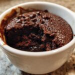 Close-up of a rich, dark chocolate mug cake with melted chocolate chips inside a white ceramic mug.