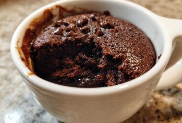 Close-up of a rich, dark chocolate mug cake with melted chocolate chips inside a white ceramic mug.