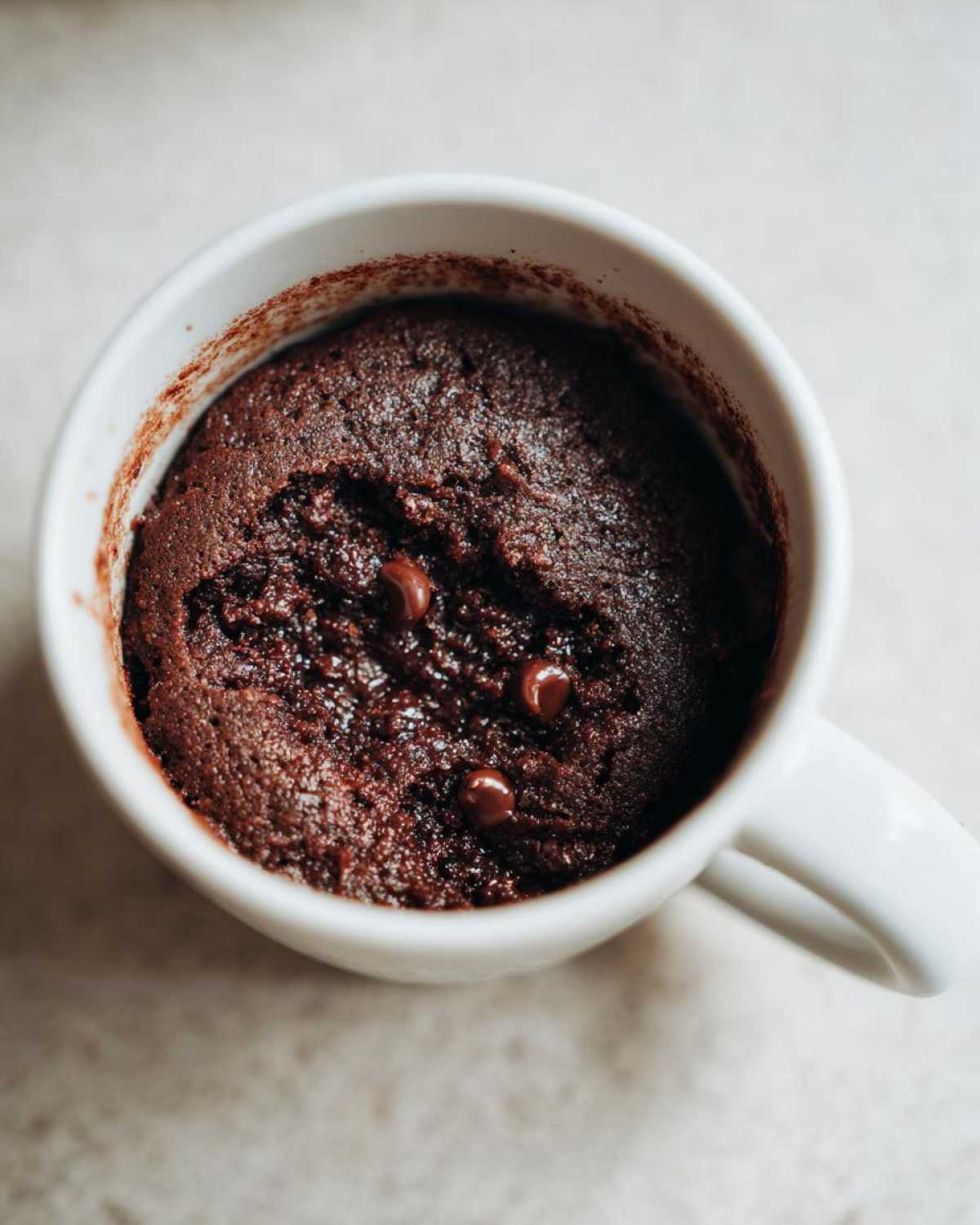 Overhead view of a rich, dark chocolate mug cake topped with chocolate chips, ready to eat.