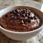 Close-up of thick, rich chocolate overnight oats topped generously with dark chocolate chips in a white bowl.