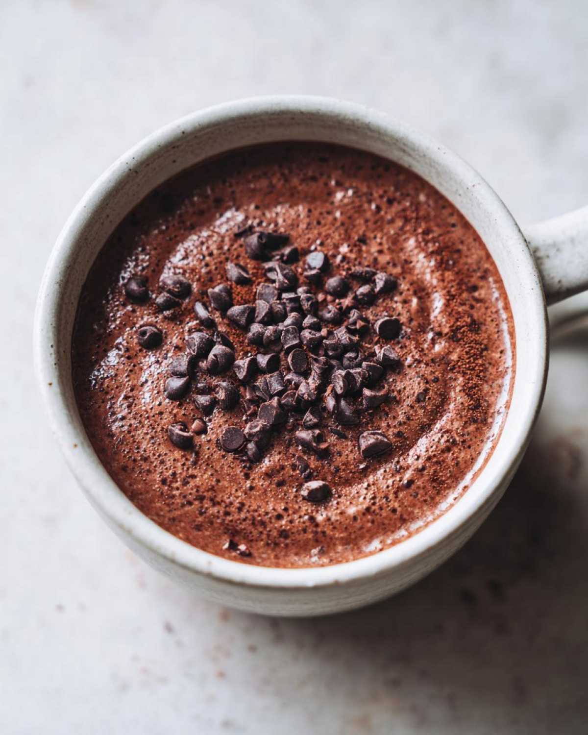 Overhead view of creamy chocolate overnight oats in a mug, topped with mini chocolate chips.