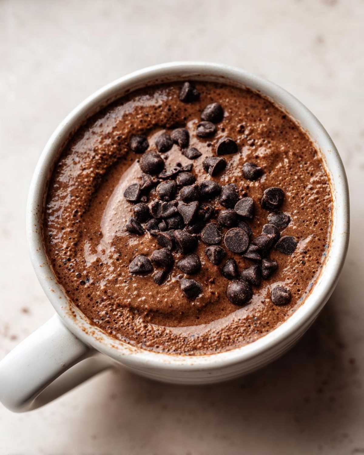 Overhead view of rich chocolate overnight oats in a white mug, topped generously with mini chocolate chips.