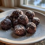 A plate of rich, chocolate-dipped pecan pie balls dusted generously with powdered sugar.