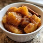 Close-up of chunky, spiced applesauce in a white bowl, garnished with a cinnamon stick.