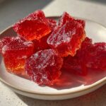 Close-up of vibrant red, crystalline chunks of homemade cinnamon rock candy resting on a small white plate.