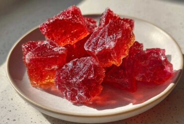 Close-up of vibrant red, crystalline chunks of homemade cinnamon rock candy resting on a small white plate.