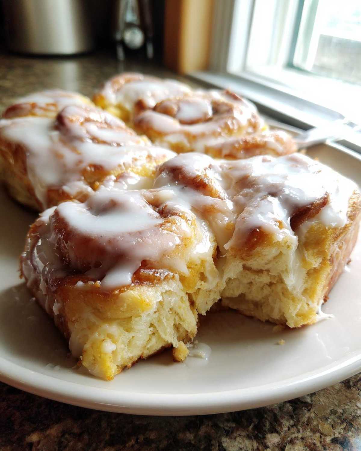 Close-up of fluffy cinnamon roll casserole pieces covered in thick white icing on a plate.