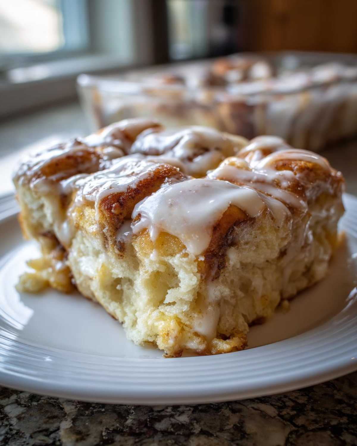 A close-up shot of a serving of fluffy cinnamon roll casserole topped with thick white icing.