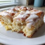 A close-up of a serving of fluffy, glazed Cinnamon roll casserole on a white plate.