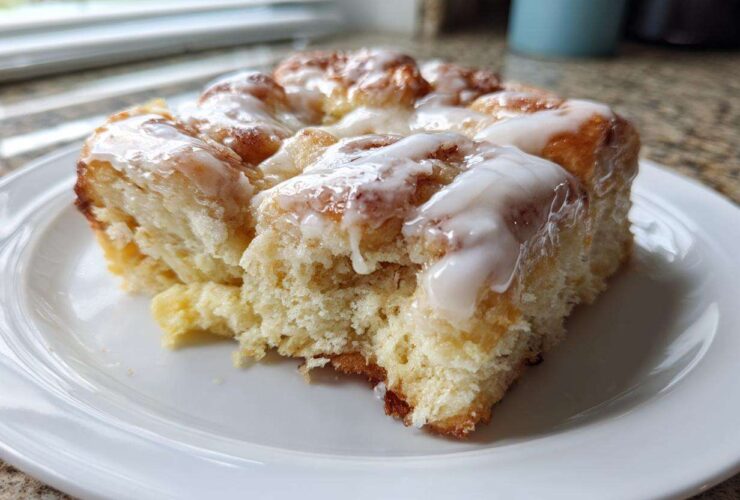 A close-up of a serving of fluffy, glazed Cinnamon roll casserole on a white plate.
