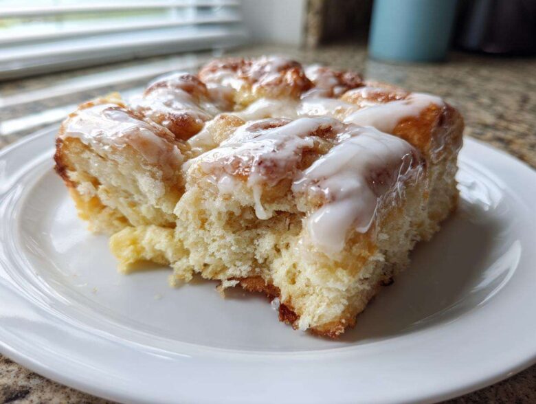 A close-up of a serving of fluffy, glazed Cinnamon roll casserole on a white plate.