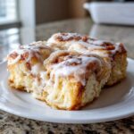 Close-up of soft, gooey squares of cinnamon roll casserole topped with thick white icing.