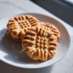 Three golden brown peanut butter cookies with classic criss-cross fork marks stacked on a white plate.