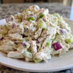 A close-up of creamy cottage cheese chicken salad mixed with celery and red onion served on a white plate.