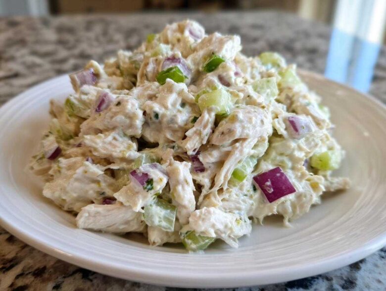 A close-up of creamy cottage cheese chicken salad mixed with celery and red onion served on a white plate.