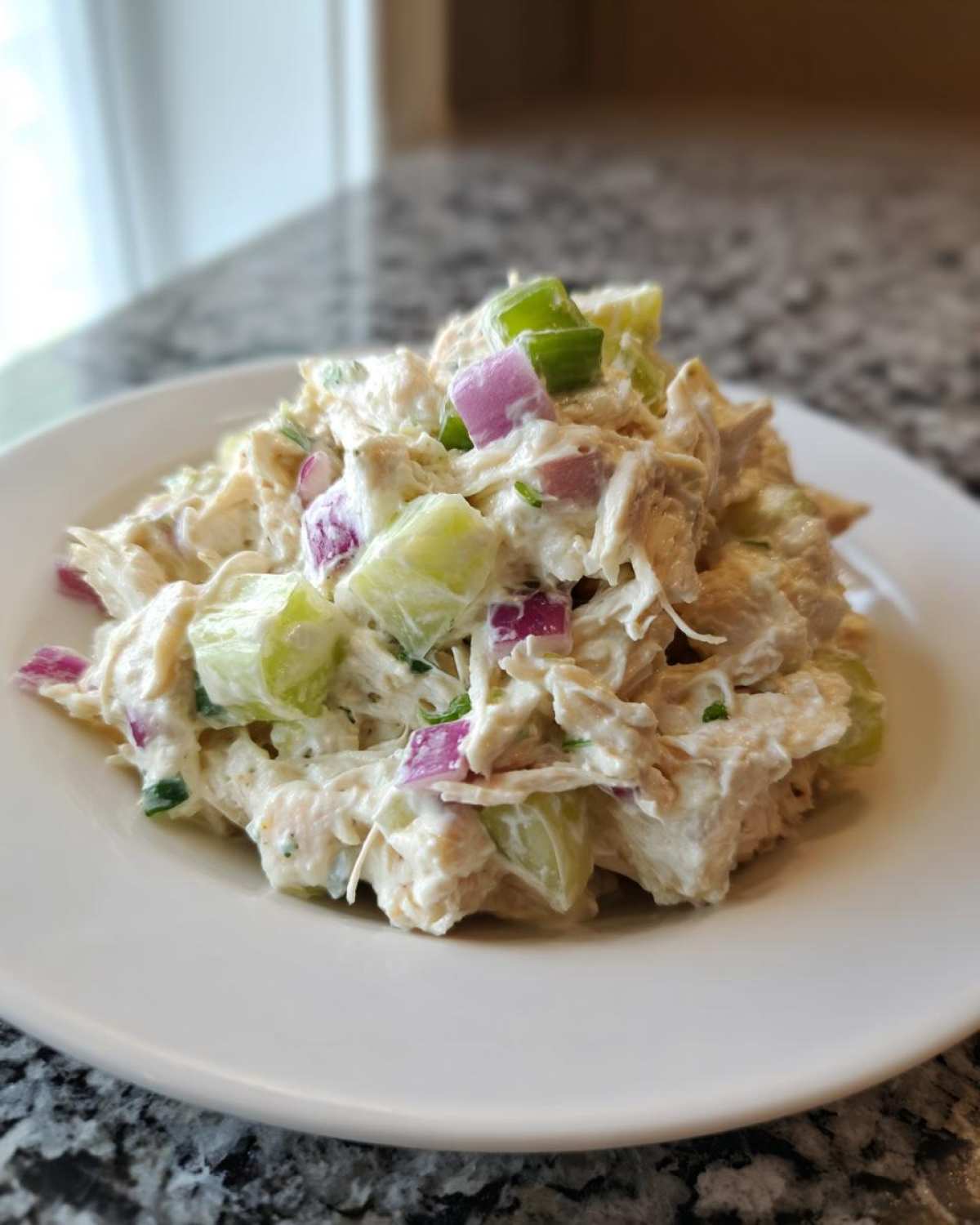 A scoop of creamy cottage cheese chicken salad mixed with chunks of cucumber and red onion on a white plate.