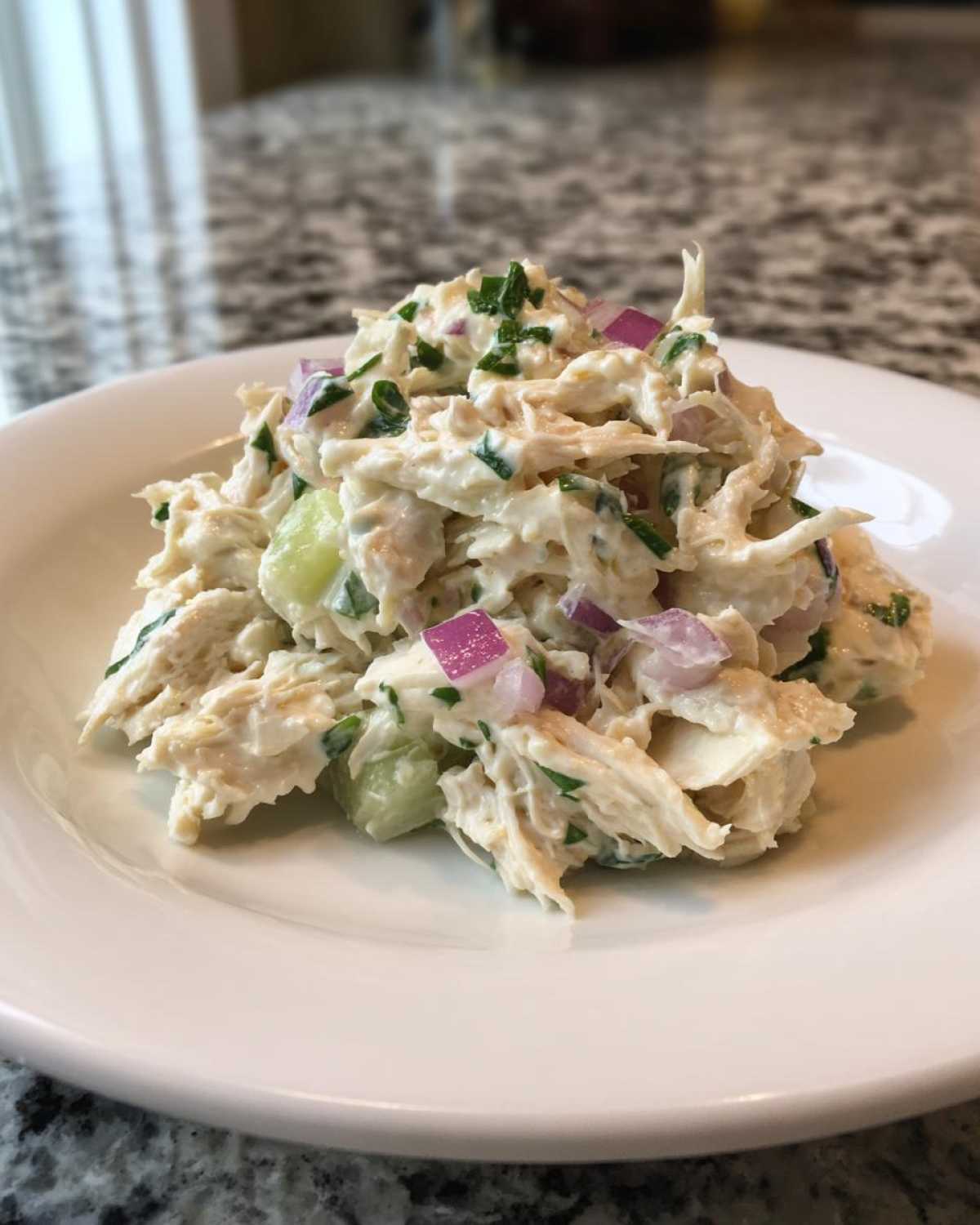 A scoop of creamy cottage cheese chicken salad mixed with diced celery, red onion, and herbs on a white plate.