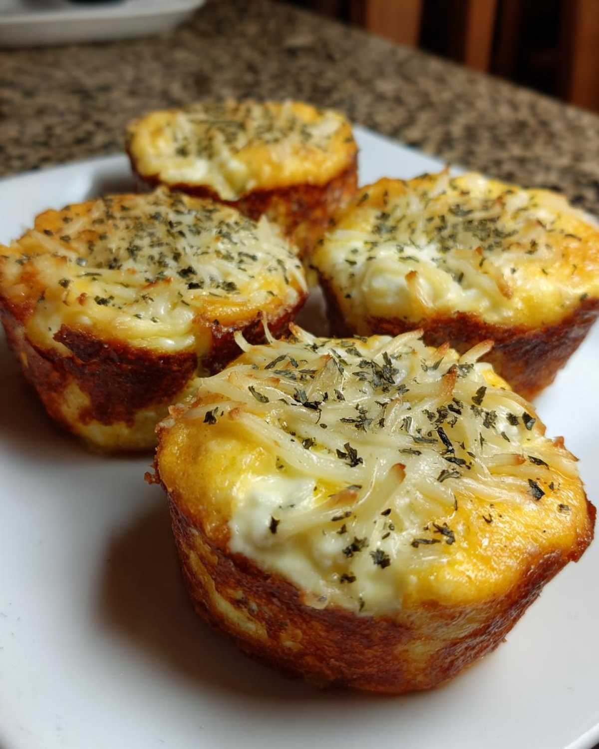 Four golden brown cottage cheese egg cups starbucks hack style, topped with melted cheese and herbs.
