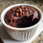 Close-up of a rich, dark chocolate Cottage Cheese Microwave Brownie in a white ramekin, topped with chocolate chips.