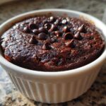 Close-up of a rich, dark chocolate Cottage Cheese Microwave Brownie topped with chocolate chips in a white ramekin.