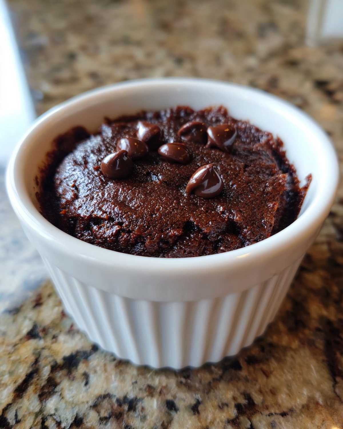A rich, dark Cottage Cheese Microwave Brownie topped with melted chocolate chips in a white ramekin.