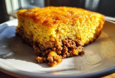 A close-up of a slice of cowboy cornbread casserole showing the thick, golden cornbread top layer over a savory ground meat filling.