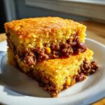 Two stacked squares of golden cowboy cornbread casserole filled with savory chili, beans, and corn.