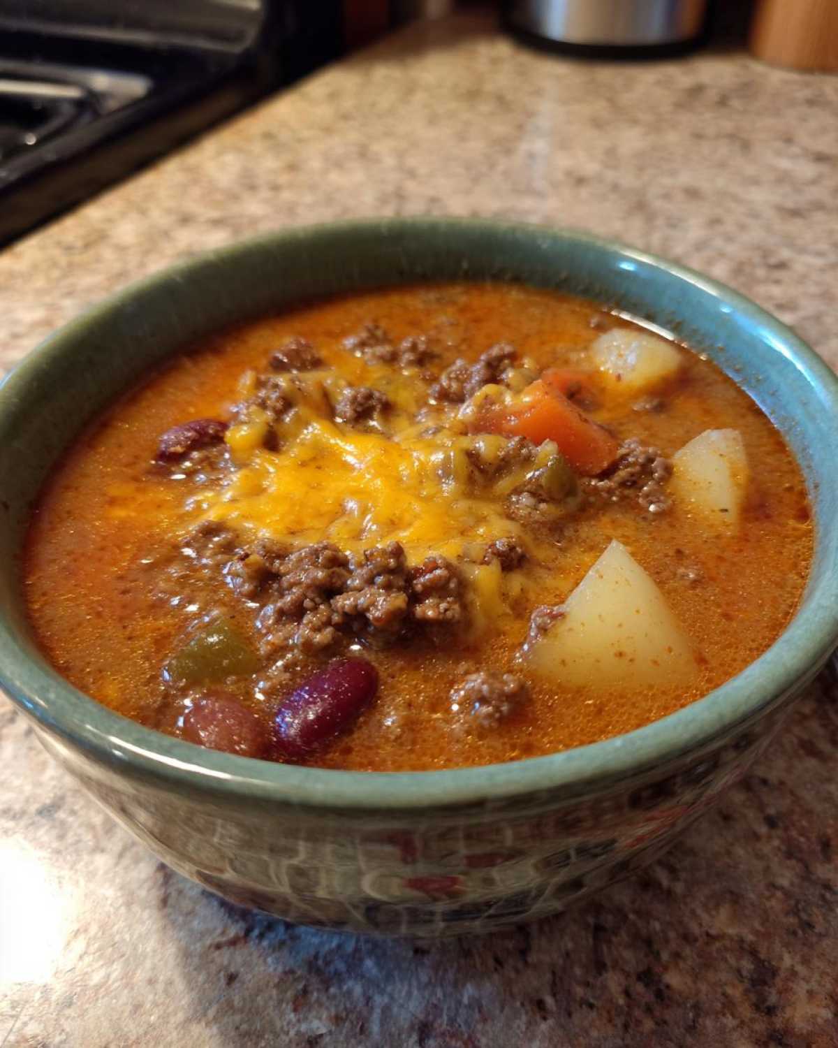 Close-up of a steaming bowl of rich cowboy soup topped with ground beef and melted cheddar cheese.