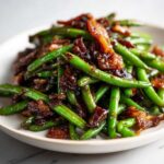 Close-up of vibrant green beans tossed in a sticky, dark glaze with crispy bacon pieces, highlighting the irresistible green beans.