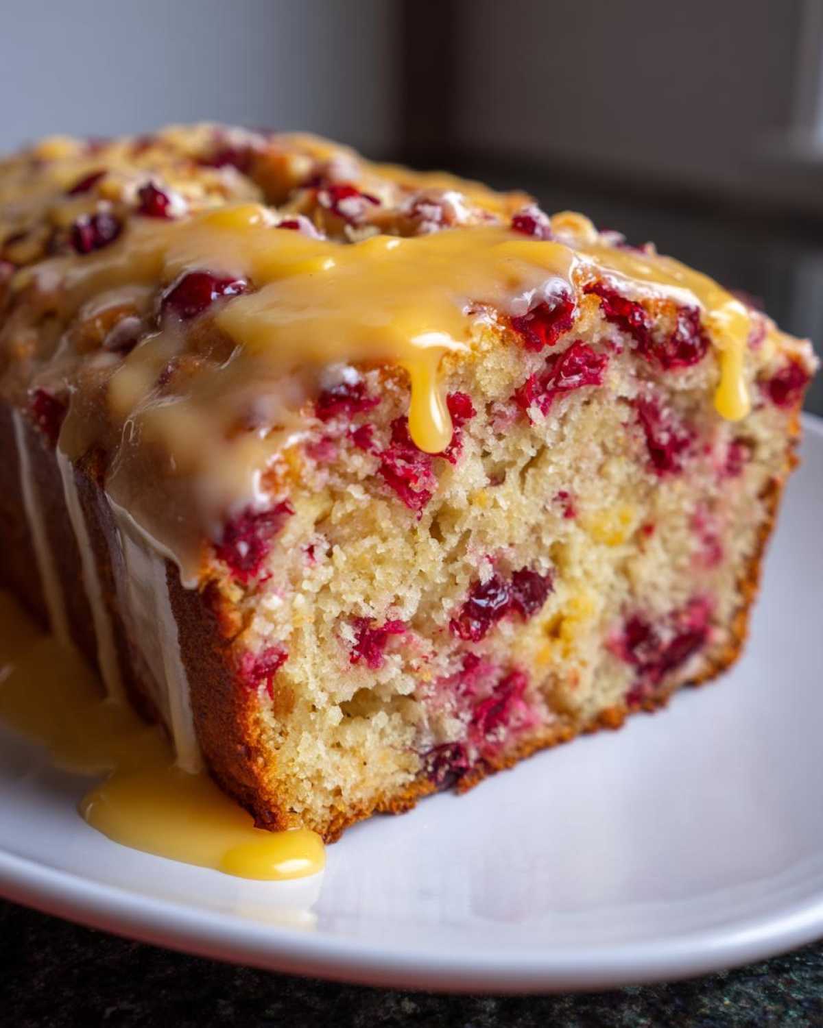 A close-up of a moist cranberry orange bread topped with a thick, dripping orange glaze.