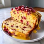 Two slices of moist cranberry orange bread topped with a thick orange glaze and fresh cranberries.