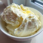 A white bowl filled with rich, creamy, pale yellow mixture, likely the base for Olive Garden Alfredo Sauce.