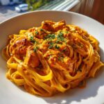 A close-up, appetizing shot of creamy cajun chicken pasta featuring fettuccine noodles coated in a rich orange sauce with chunks of seasoned chicken, garnished with parsley.
