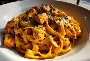 A close-up shot of rich, orange-hued creamy cajun chicken pasta tossed with fettuccine and topped with seasoned chicken pieces and parsley.
