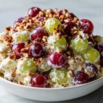 Close-up of a creamy chicken salad chick grape salad mixture with red and green grapes and chopped pecans.