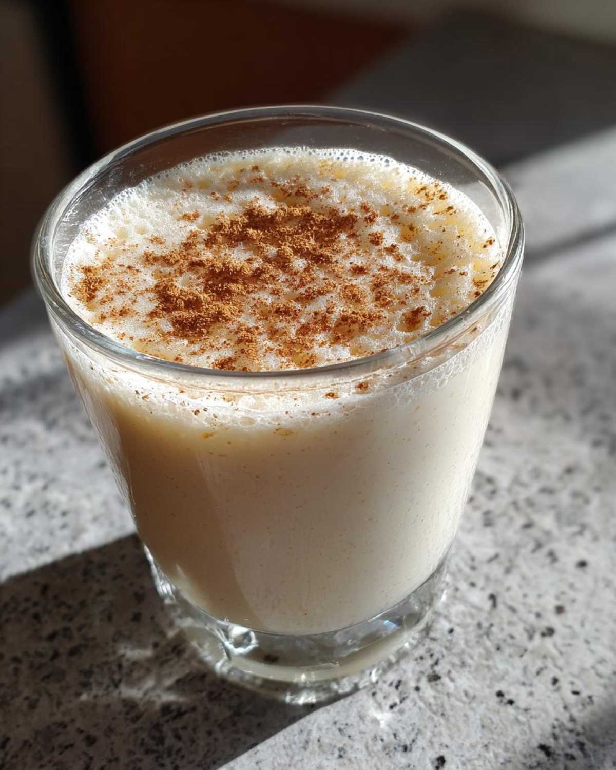 Close-up of a glass filled with creamy coquito recipe, garnished with a dusting of cinnamon on top.