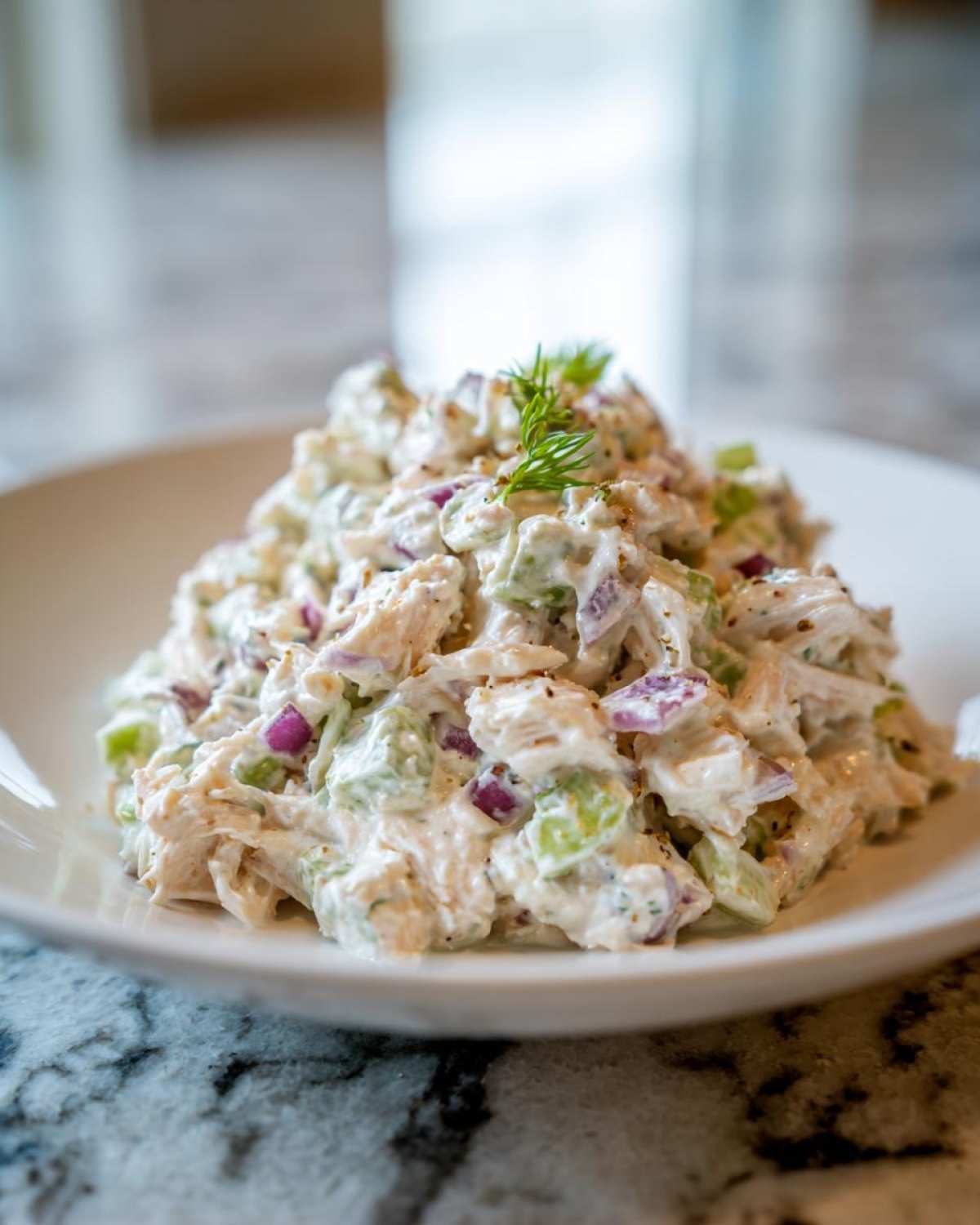 A mound of creamy cottage cheese chicken salad mixed with celery and red onion, garnished with dill.