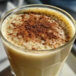Close-up of a creamy glass of homemade eggnog topped generously with ground cinnamon.