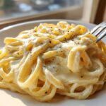 Close-up of fettuccine pasta coated in rich olive garden alfredo sauce, topped with black pepper, with a fork lifting some noodles.