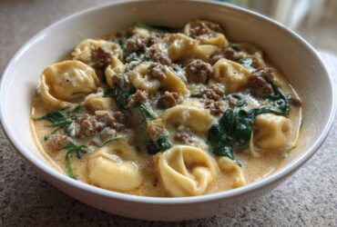A close-up of a hearty bowl of creamy italian sausage tortellini soup with spinach.