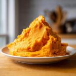 A large, fluffy mound of bright orange mashed sweet potatoes served on a white plate.