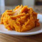 A close-up of a fluffy mound of bright orange mashed sweet potatoes topped with melted butter.